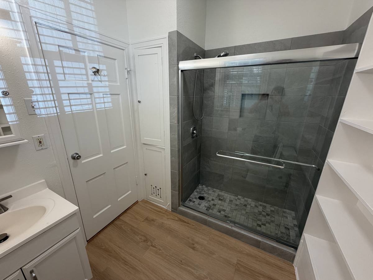 Renovated bathroom with a grey-tiled walk-in shower, glass sliding doors and mosaic tile floor