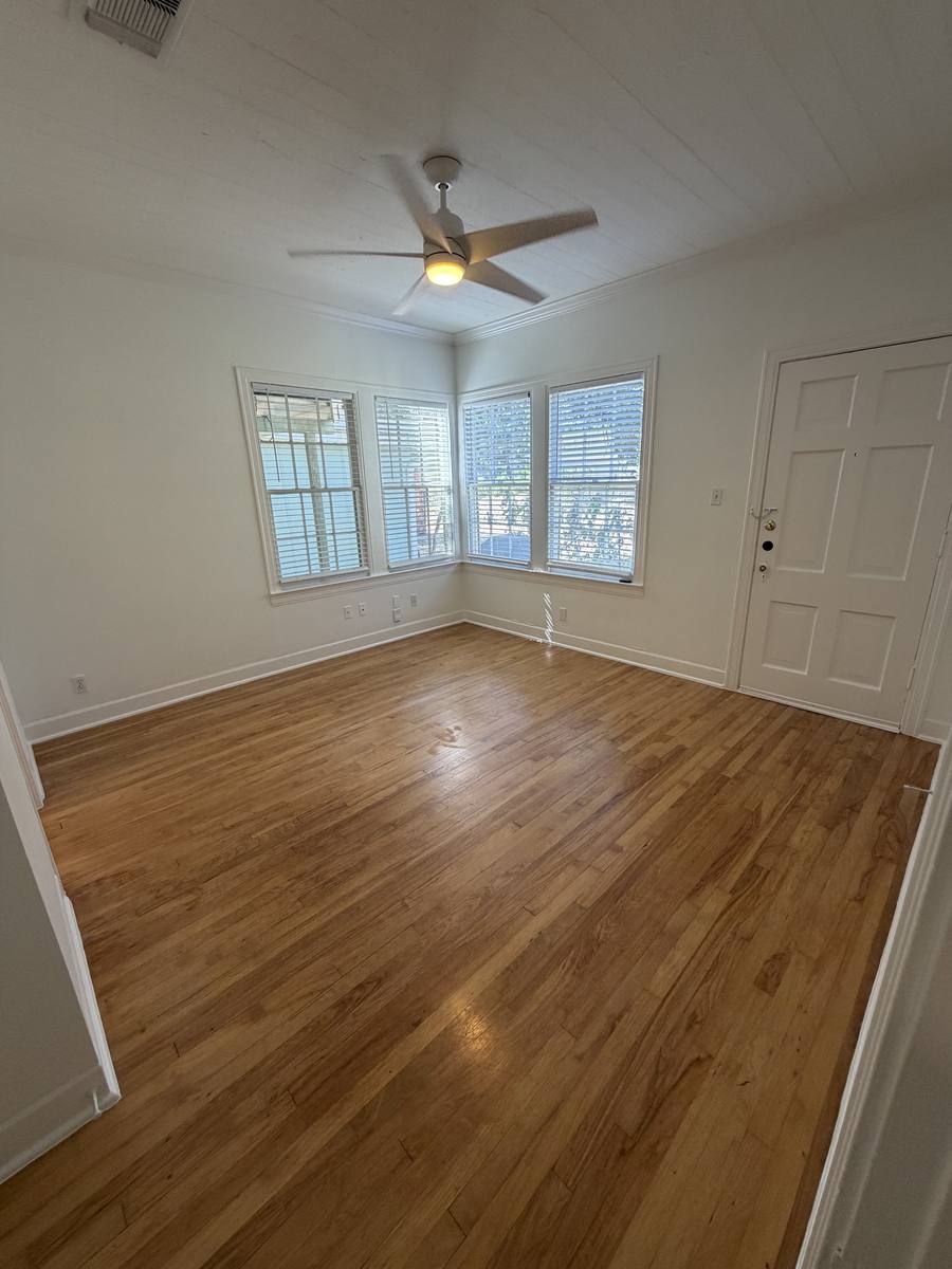 Bedroom of Unit D — bright corner room with original hardwood floors, ceiling fan and three windows