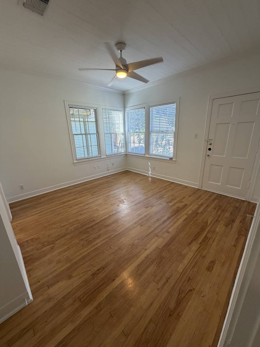 Bedroom of Unit D — bright corner room with original hardwood floors, ceiling fan and three windows