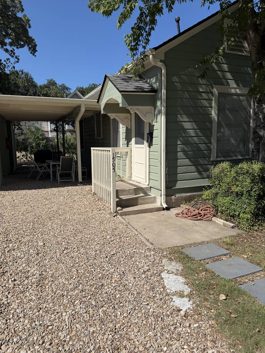 Sage green cottage exterior of Unit D with covered carport and shaded outdoor seating
