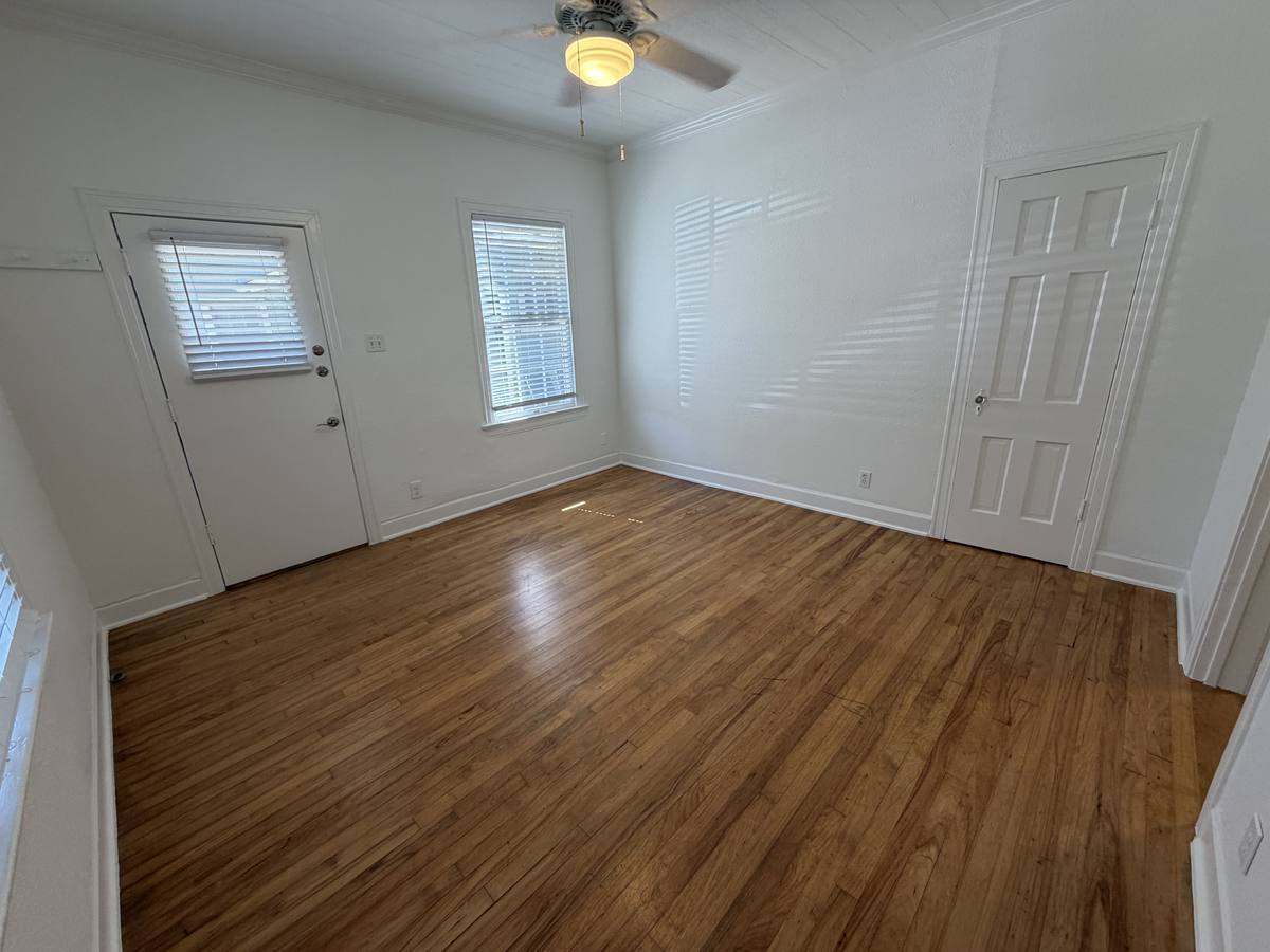 Living room of Unit D with original hardwood floors, ceiling fan and a private exterior door